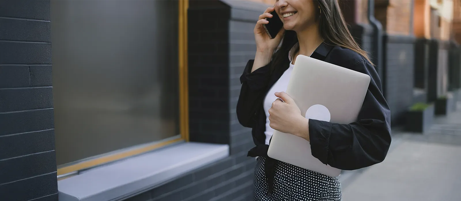 Woman holding a laptop and talking on the phone on her way to work, represents how you can contact Susan Podbielski to start therapy that fits your busy life.