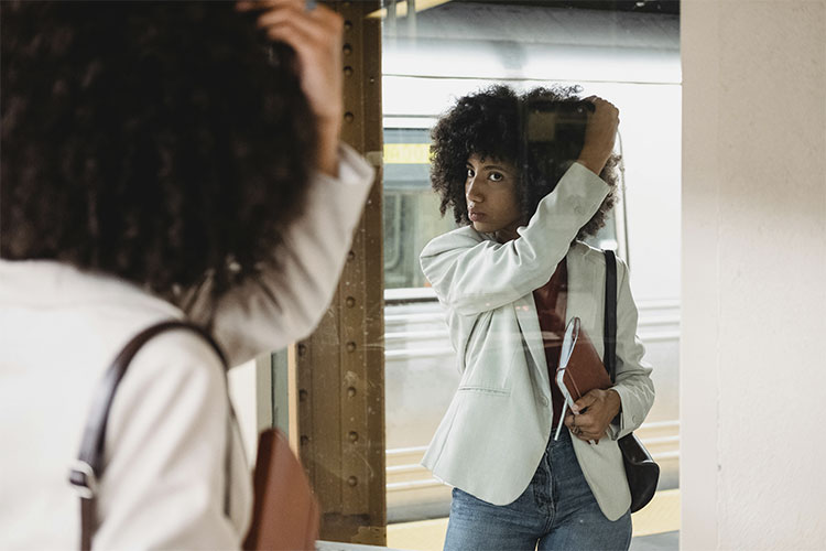 Woman waiting for the subway while fixing her her, represents smart women's perfectionism and secret sabotage.