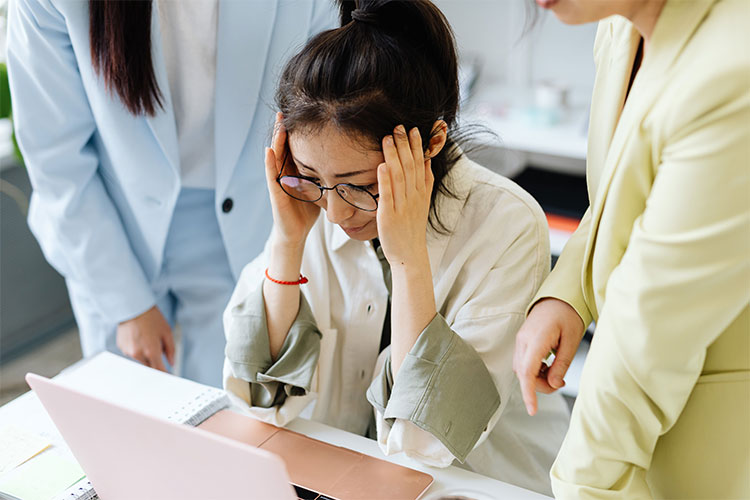 Woman with her hands on her head, looking worried while surrounded by coworkers, represents the stigma of failure.