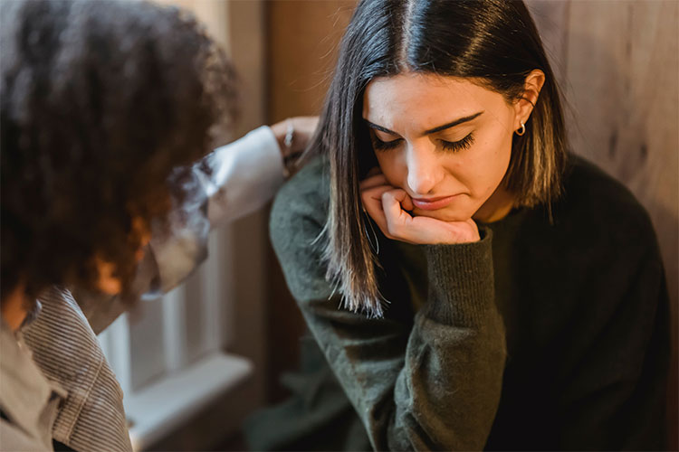 Woman comforts a friend experiencing sorrow, represents how you can cope with survivor's guilt after losing a sibling.